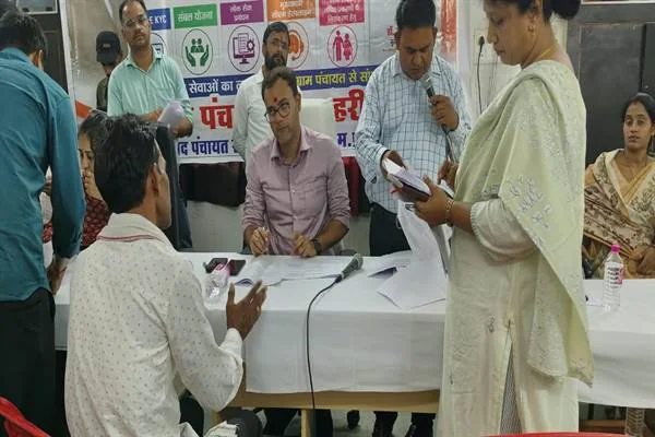 शिविर में मेज के सामने बैठा आवेदक अपनी बात बता रहा है और अधिकारी दस्तावेज देख रहे हैं